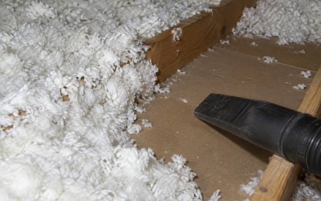 Close view of a black vacuum hose resting on loose white insulation next to a joist
