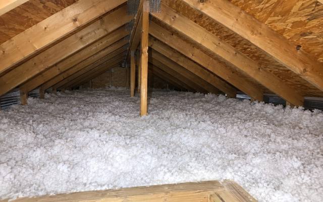 Thick white blown-in insulation filling an attic up to the side of a raised wooden hatch frame